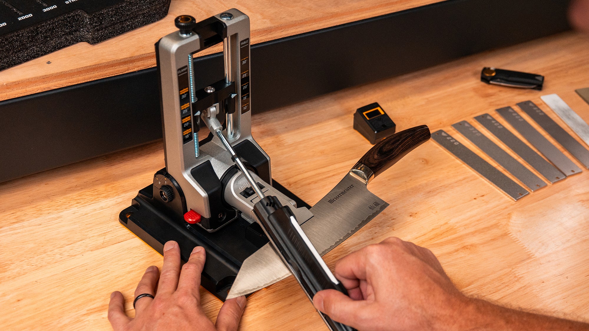 Live view of Professional Precision Adjust Elite sharpening a kitchen knife with abrasive set in background.