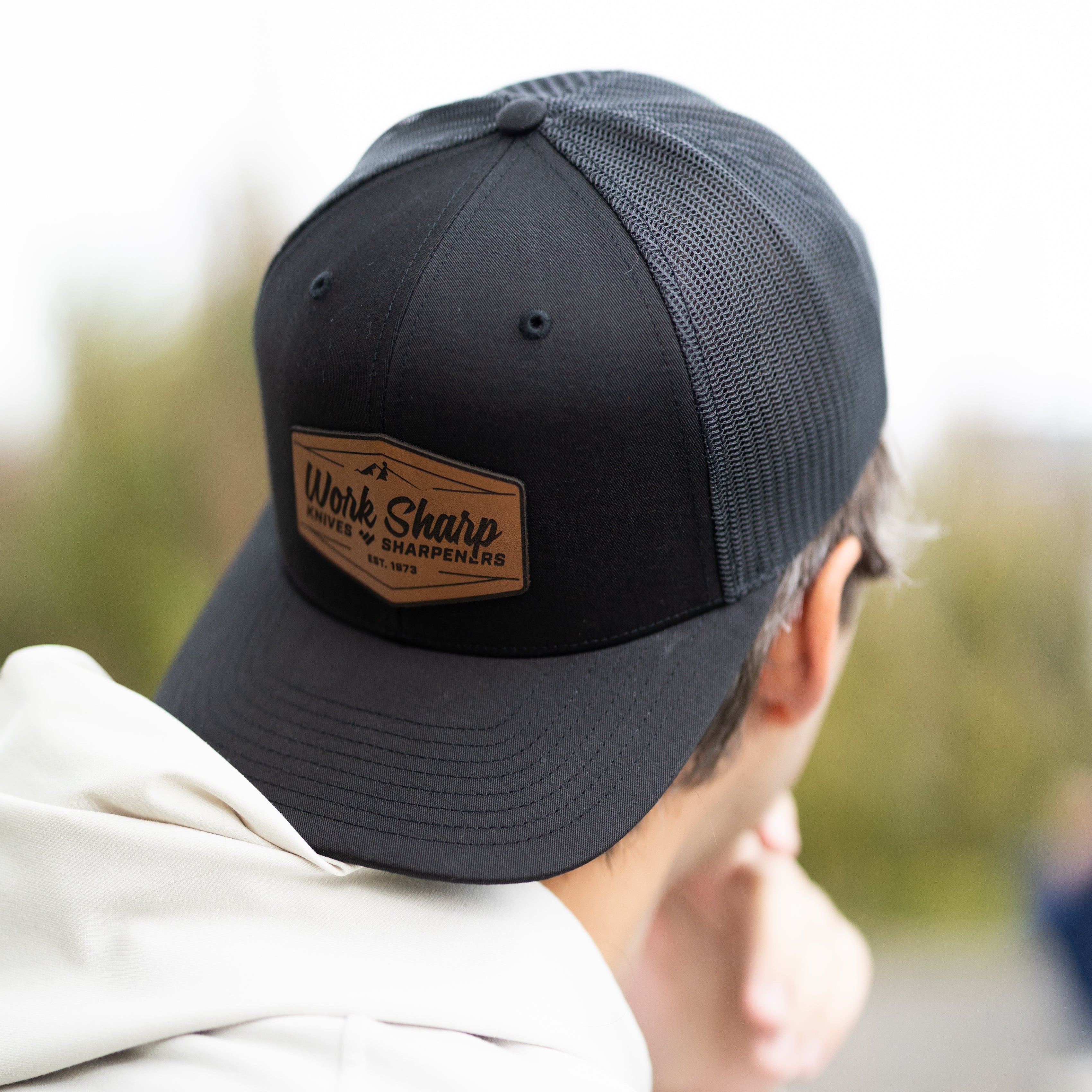 Person wearing a Work Sharp black cap with a leather patch, blurred background