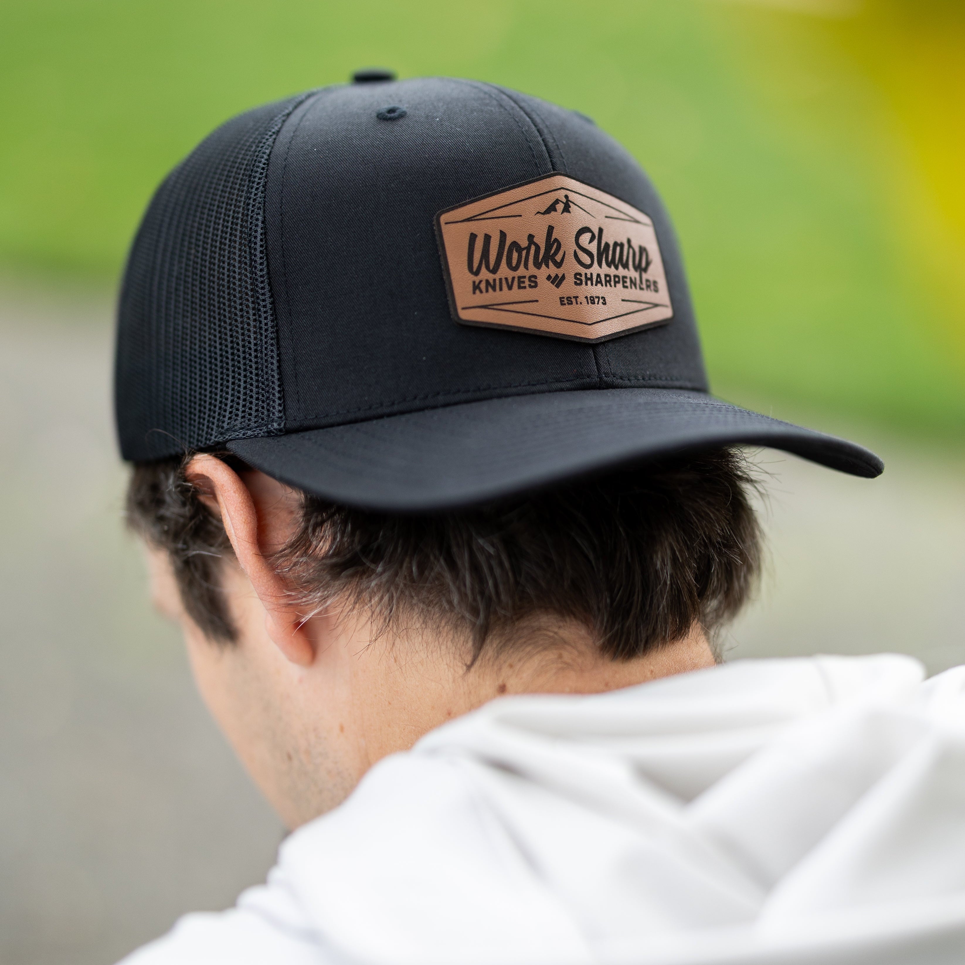 Person wearing a Work Sharp black cap with a leather patch in an outdoor setting