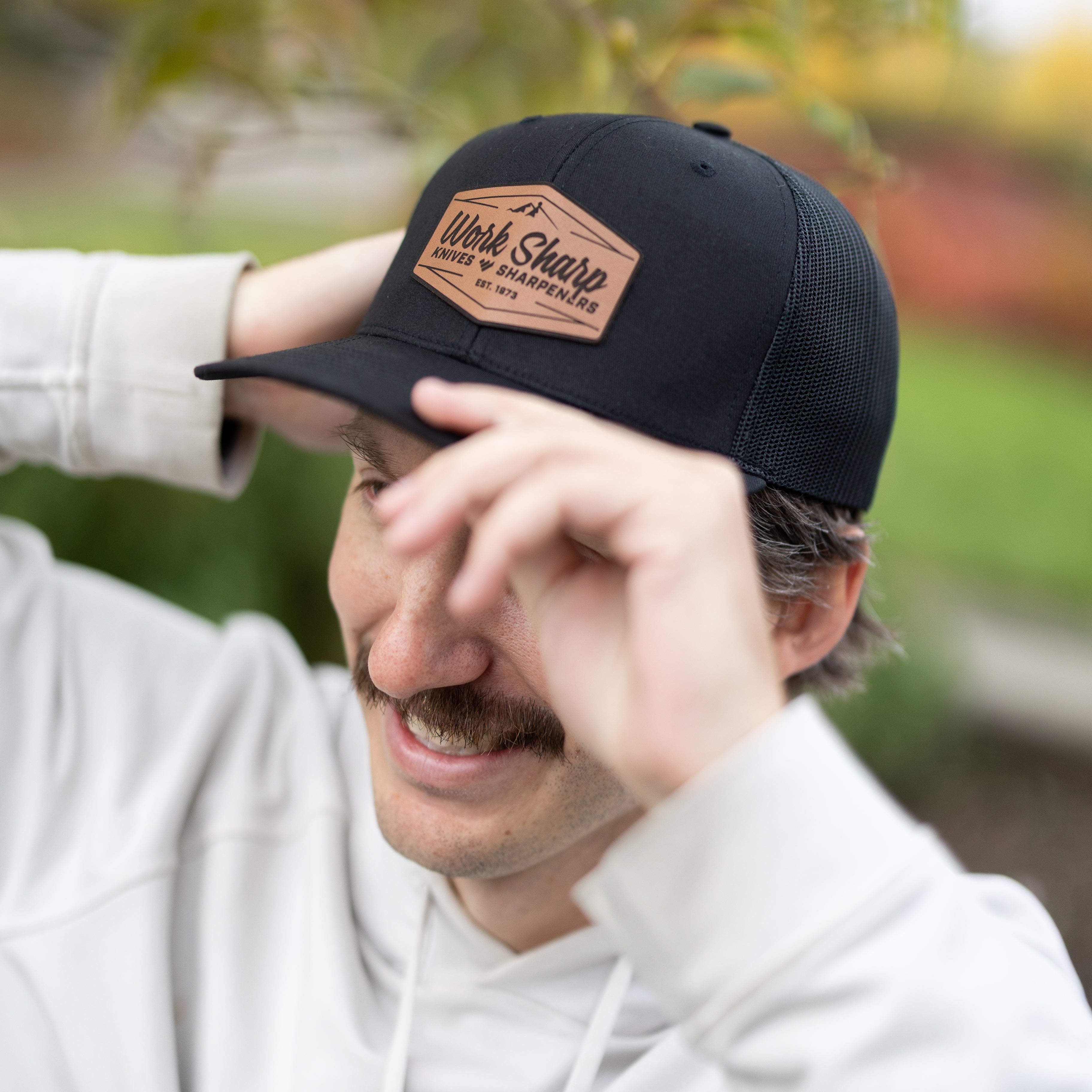 Person wearing a Work Sharp black cap with leather patch outdoors