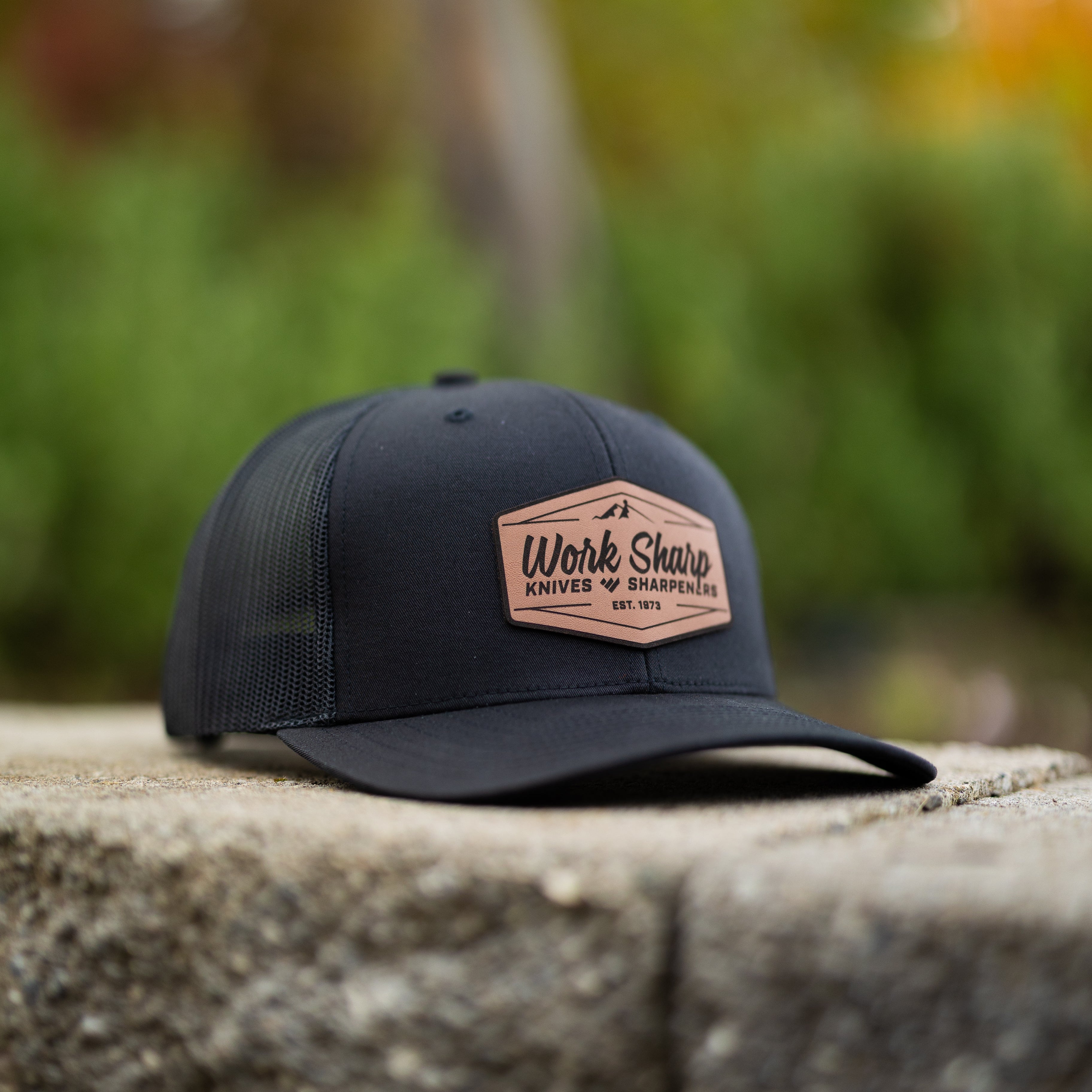 Work Sharp Black cap with a leather patch on a stone surface with a blurred natural background