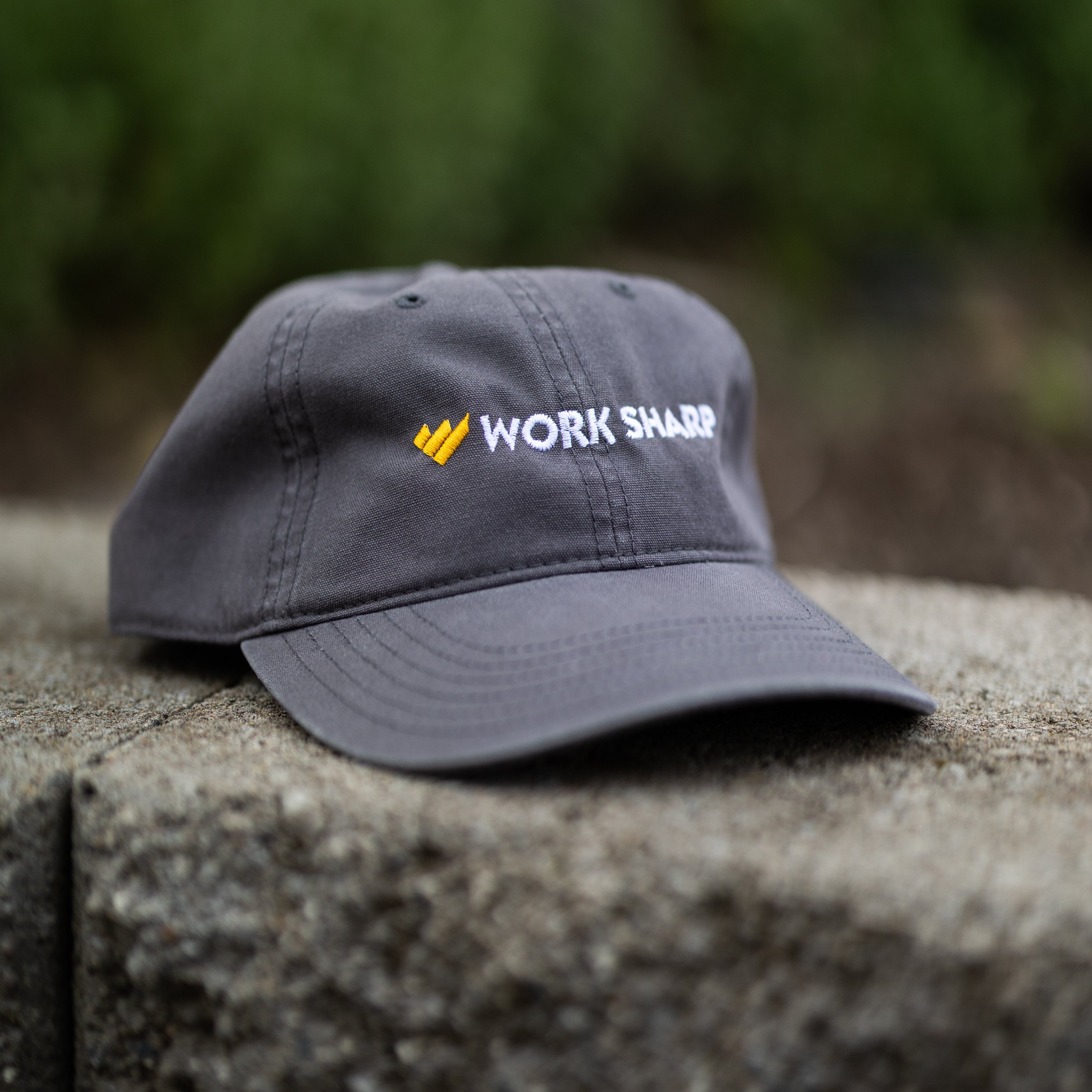 Gray cap with 'Work Sharp' logo on a stone surface with blurred greenery in the background