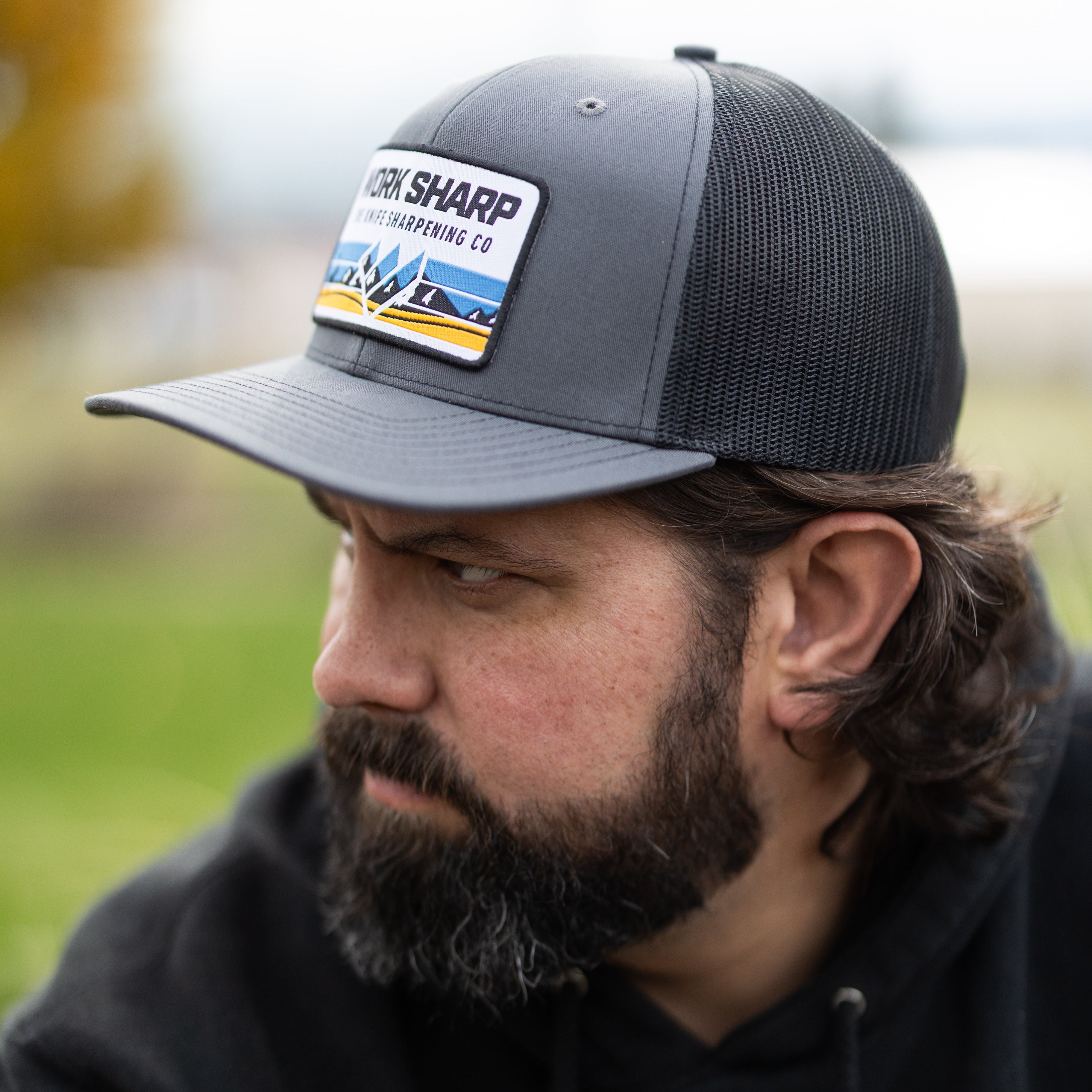 Man wearing a gray cap with a Work Sharp logo and a black hoodie with a logo, outdoors.