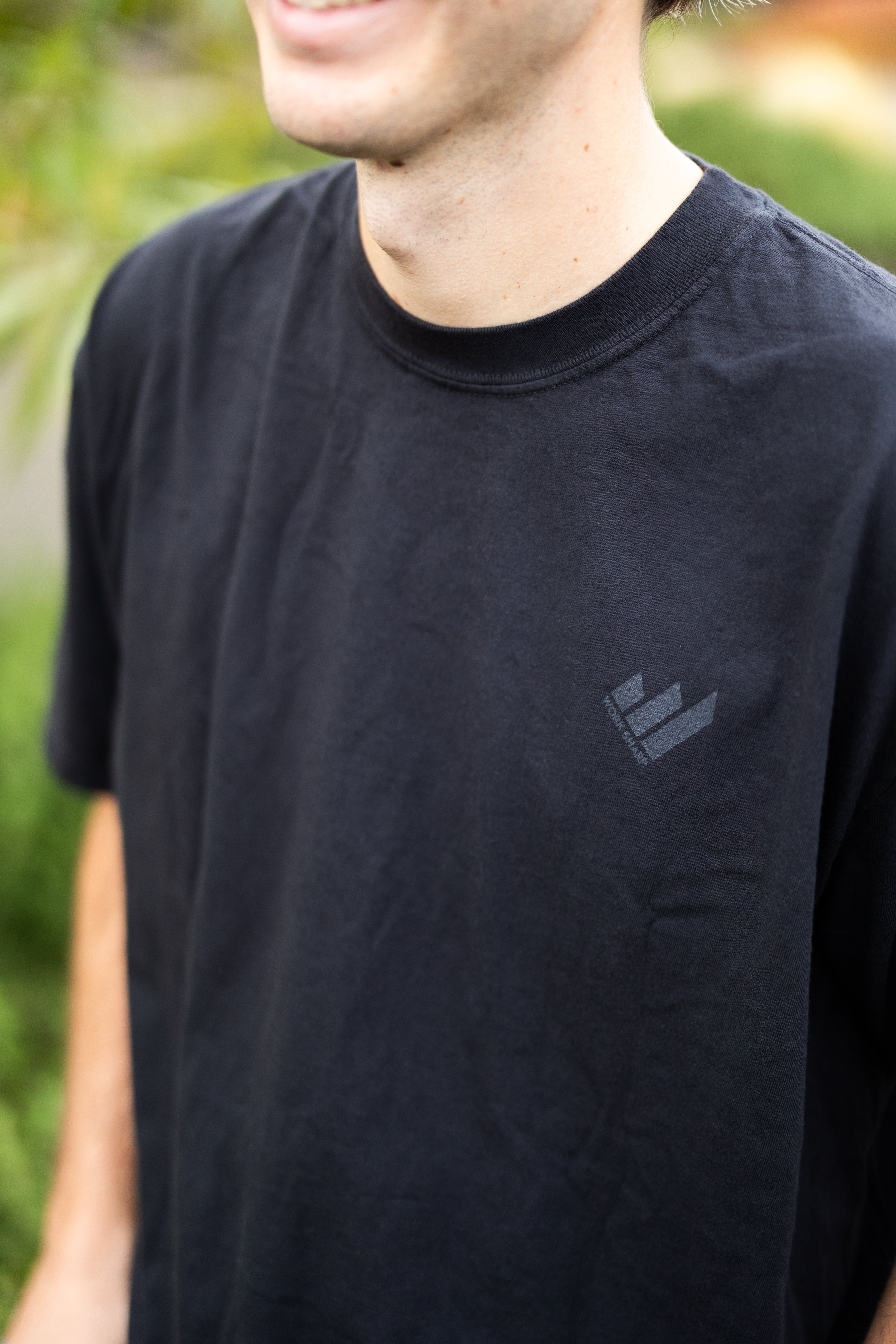 Person wearing a Work Sharp Death Before Dull Knives black t-shirt with a logo on a blurred natural background