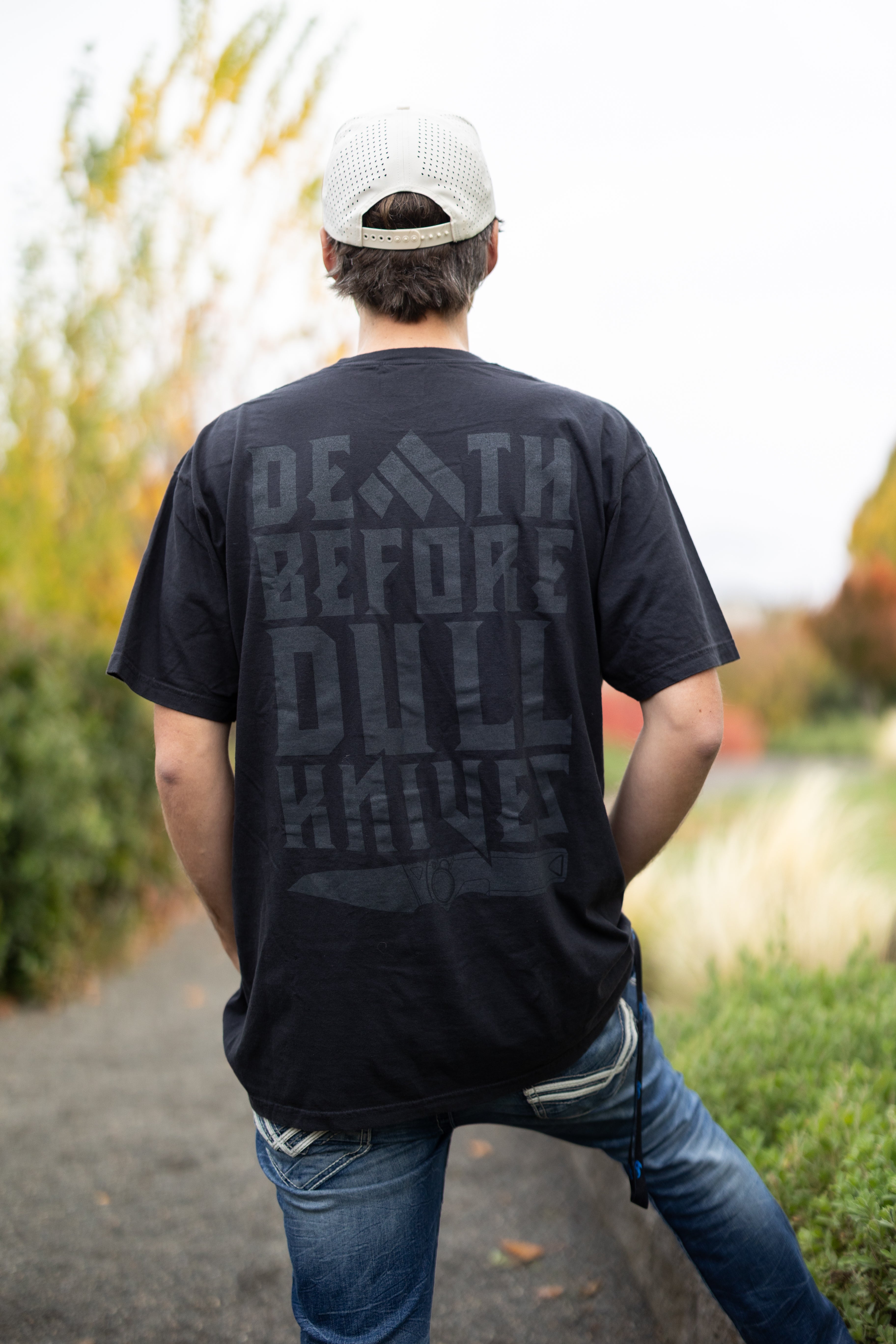 Person wearing a Work Sharp Death Before Dull Knives black t-shirt with text on the back, standing outdoors.