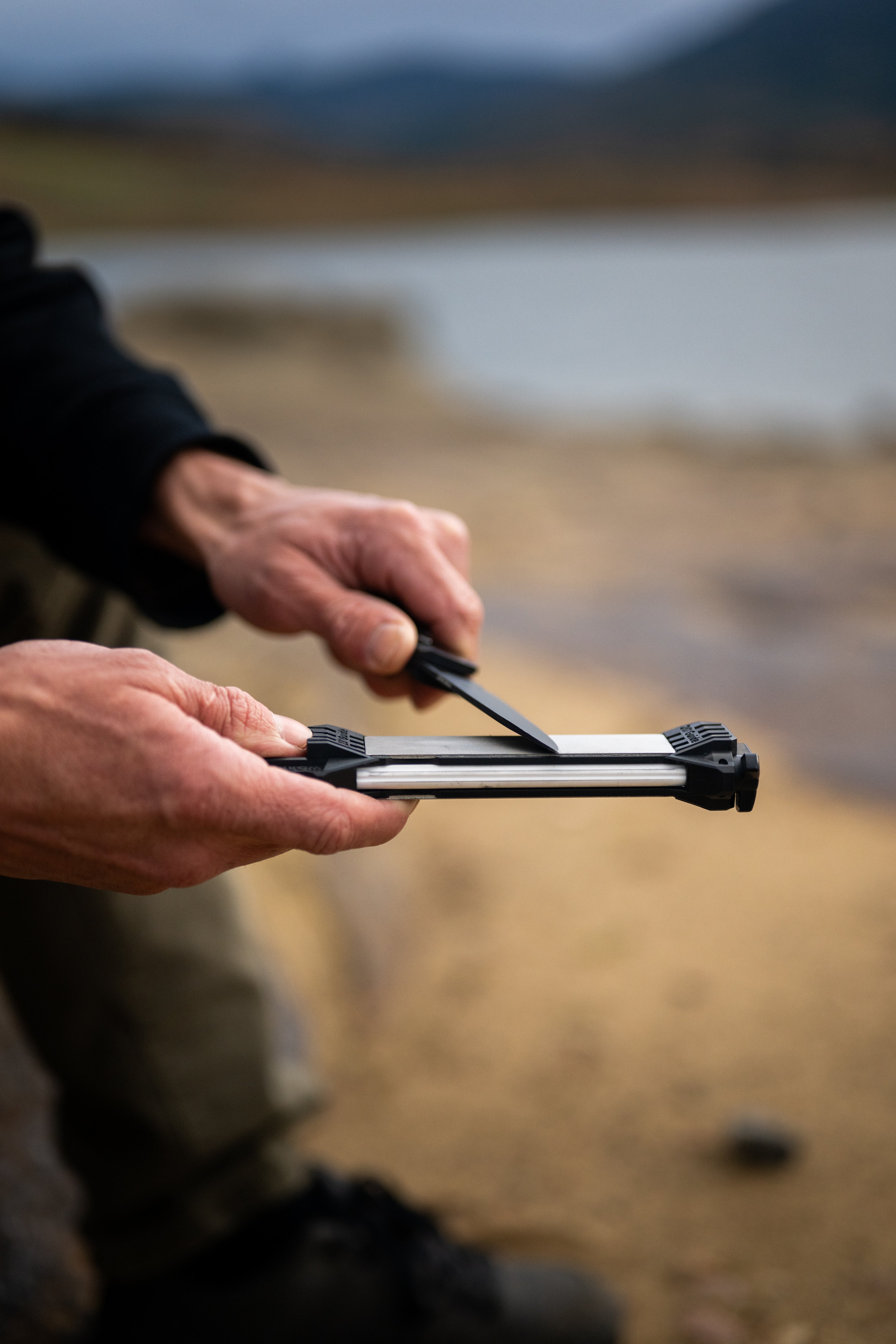 Person using a folding knife and a Guided Field Sharpener Blackout | Reserve Series outdoors with a blurred natural background