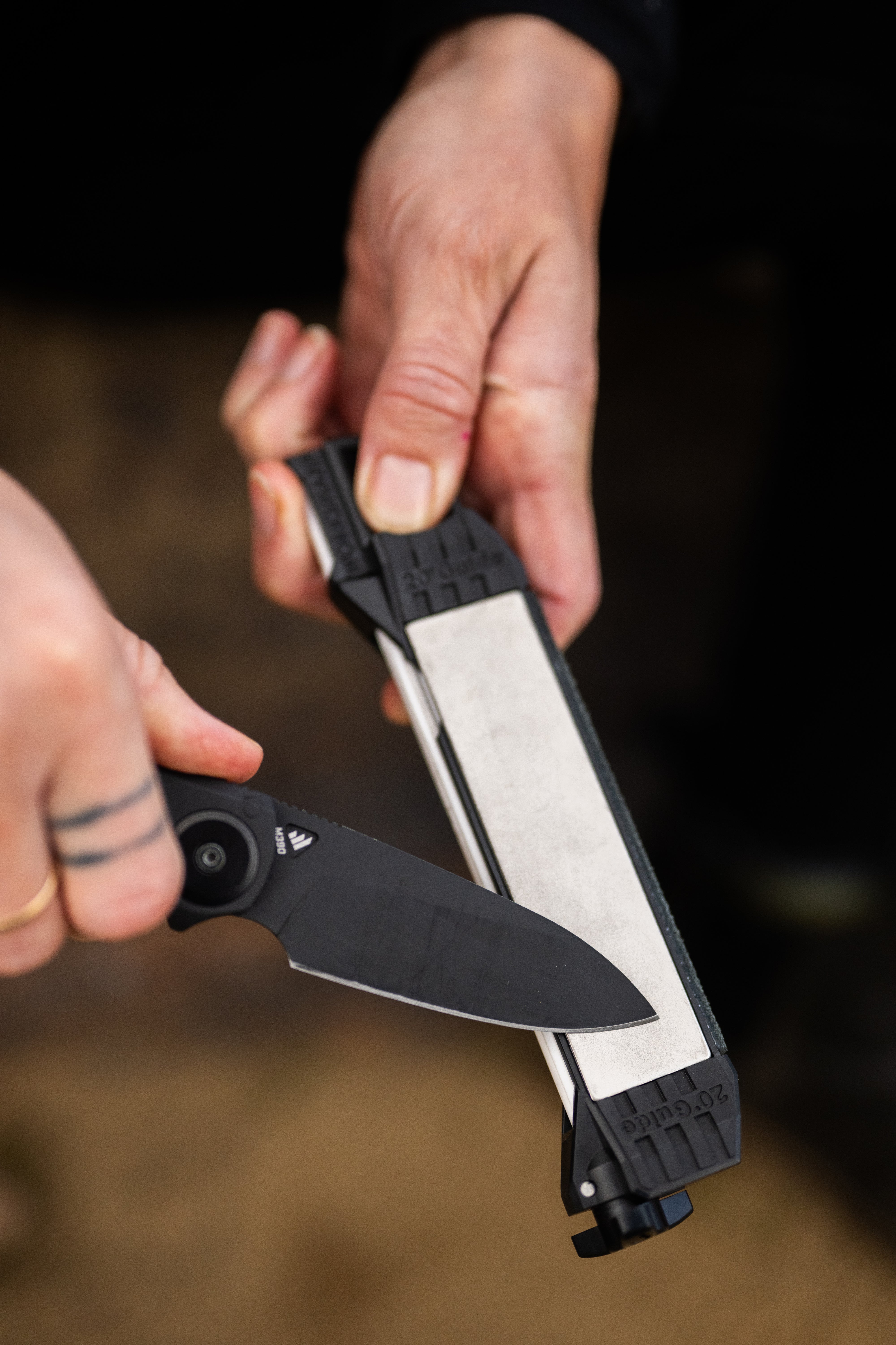 Close-up of a person holding a folding knife and a Guided Field Sharpener Blackout | Reserve Series with a blurred background